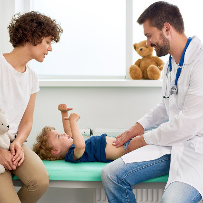 Portrait of smiling doctor examining stomach of little boy and asking him to say where it hurts